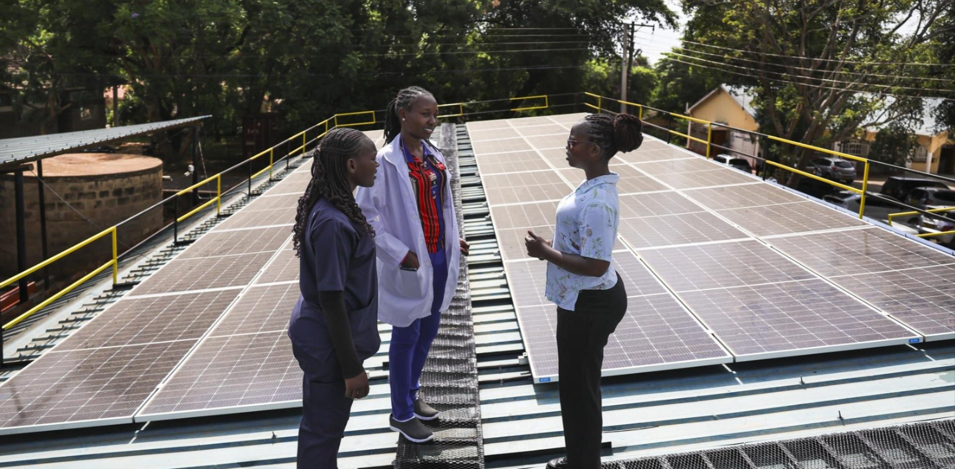 Three health workers talking on a hospital roof covered in solar panels in Makueni County, Kenya